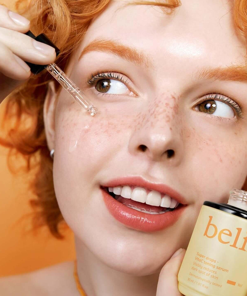 Woman applying BELIF Super Drops Vita C Toning Serum 30ml to her face with dropper from the bottle.
