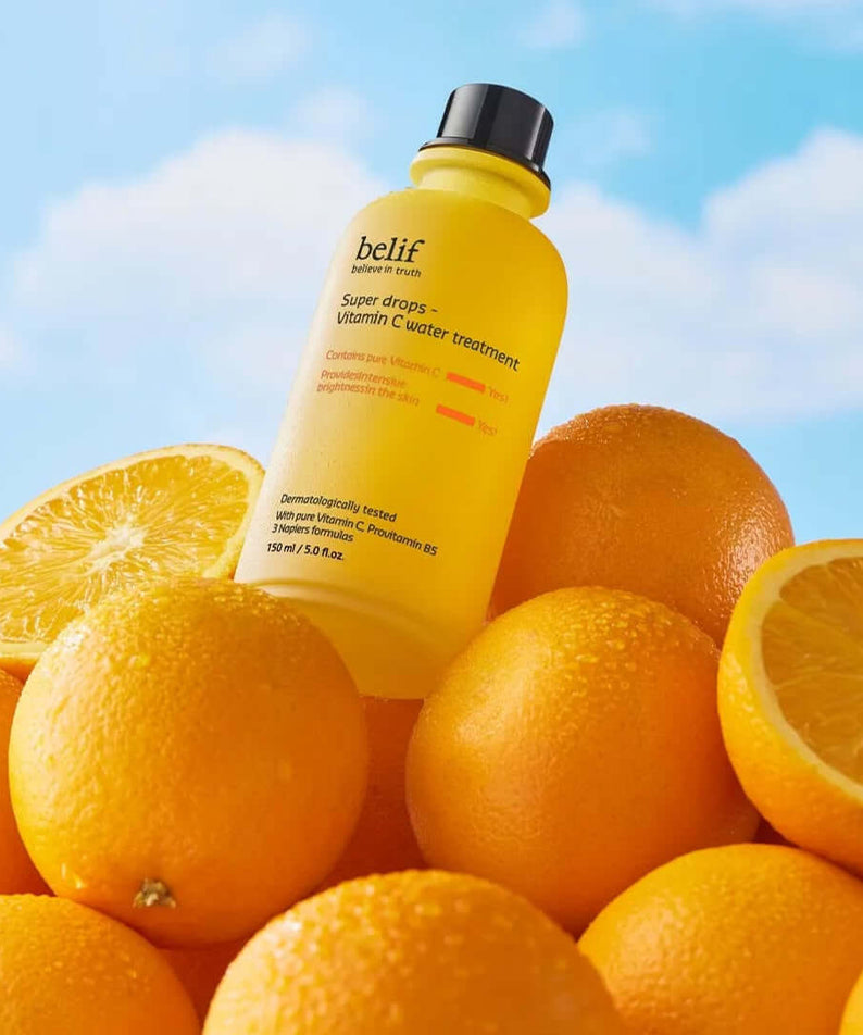 BELIF Super Drops-Vitamin C Water Treatment 150ml bottle surrounded by fresh oranges against a blue sky background
