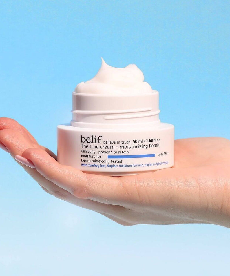Person holding BELIF The True Cream Moisturizing Bomb 50ml jar with creamy texture, illustrating skincare product's moisturizing benefits.