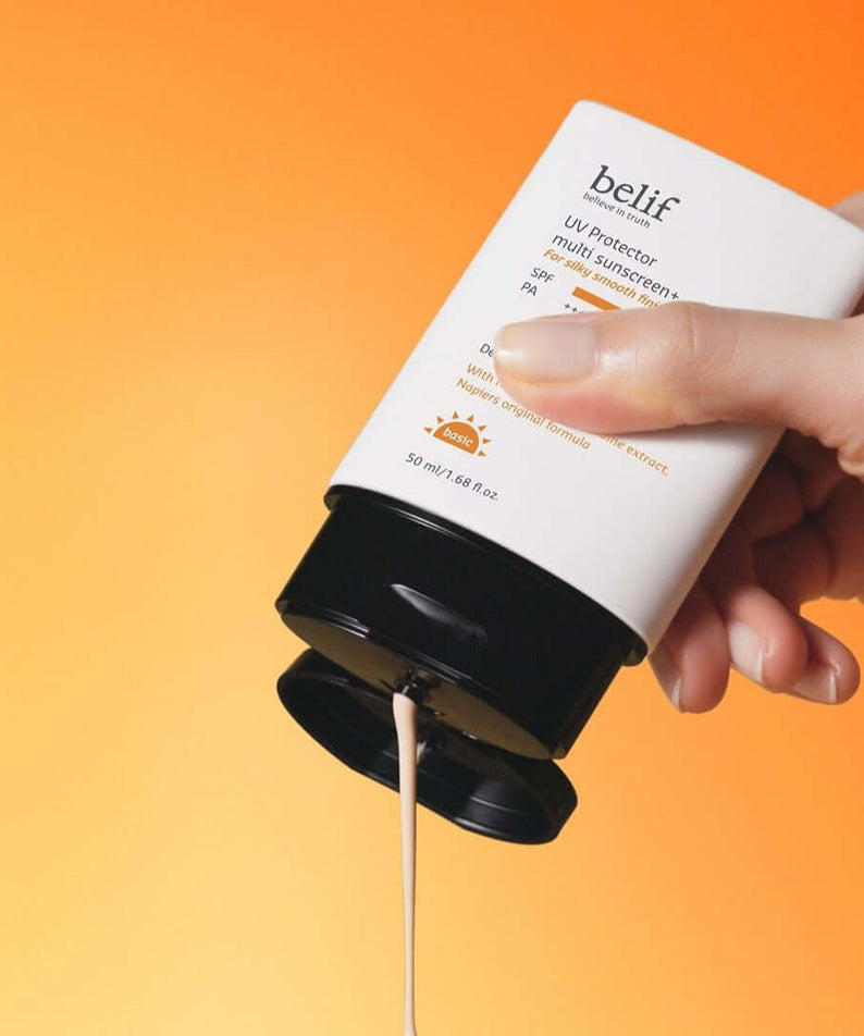 Hand holding BELIF UV Protector Multi Sunscreen Plus 50ml against orange background.