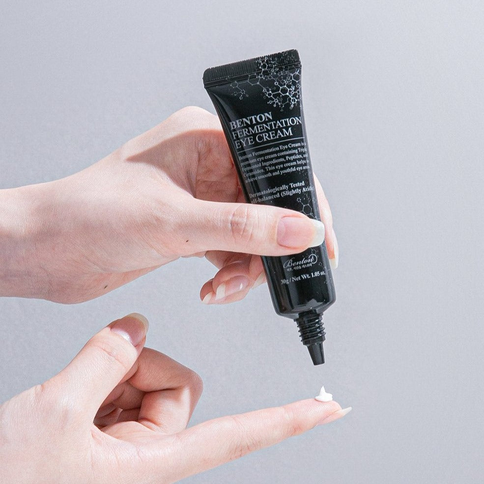 Person applying BENTON Fermentation Eye Cream 30ml, rich in peptides and ceramides, for anti-aging and elasticity around eyes.
