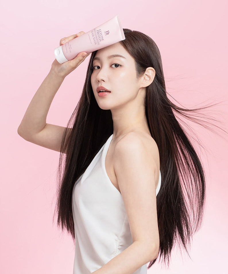 Woman holding BENTON Glycine Protein Deep Conditioning Hair Mask 220ml on a pink background, showcasing smooth and shiny hair