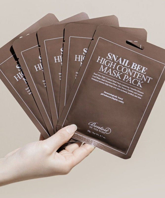 Hand holding BENTON Snail Bee High Content Mask Pack sheets in a fan arrangement