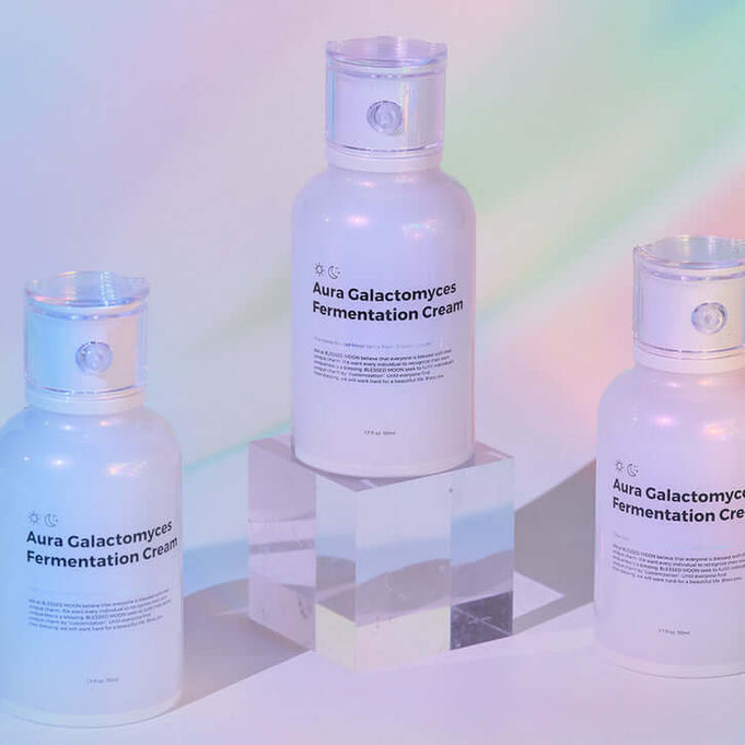 BLESSED MOON Aura Galactomyces Fermented Cream 50ml bottles displayed on a clear pedestal with pastel background