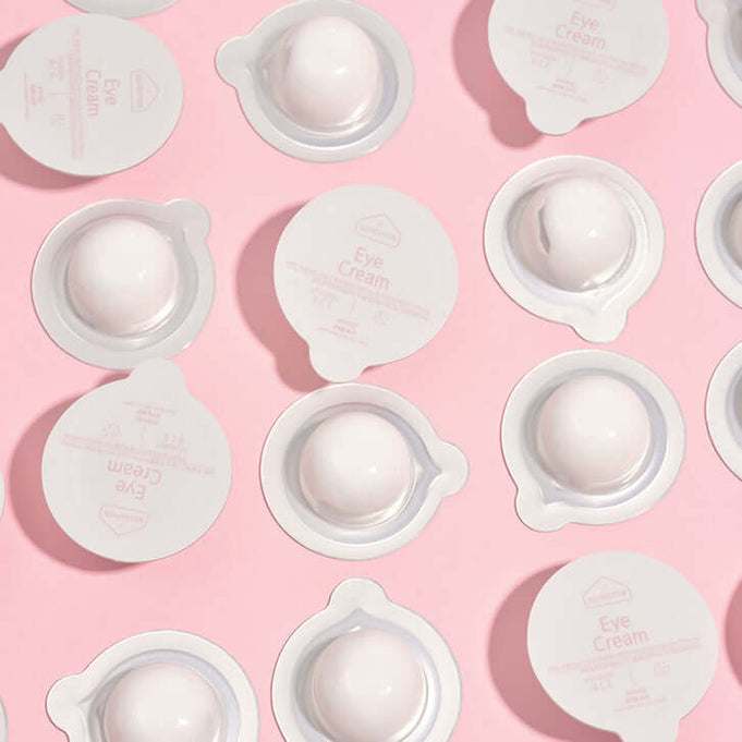 BLESSED MOON Eye Kit eye cream pods on a pink background, showcasing the elegant packaging and design.