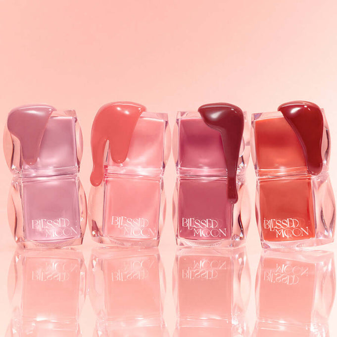 Assorted shades of BLESSED MOON Veil Glow Lip Tint in transparent containers against a pink background.