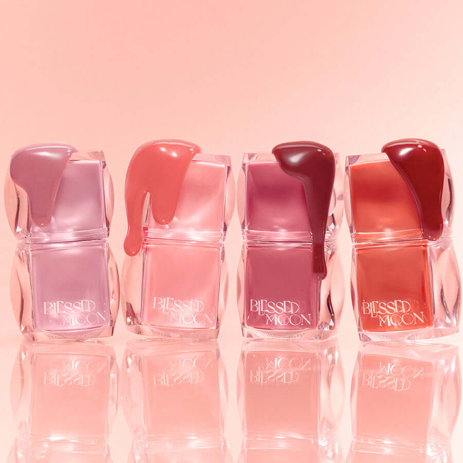 Assorted shades of BLESSED MOON Veil Glow Lip Tint in transparent containers against a pink background.