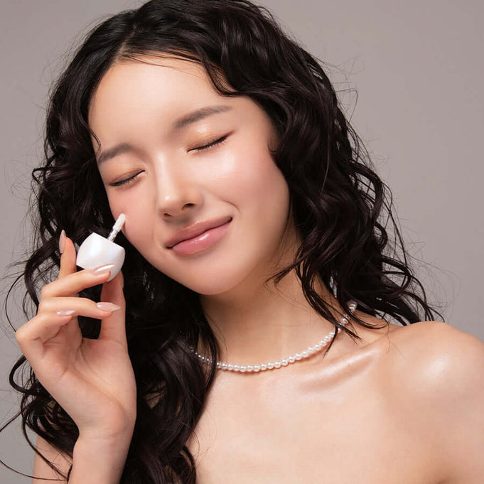 Woman applying BLESSED MOON Veil Melting Glass Highlighter to her cheek, demonstrating a radiant and glowing makeup look