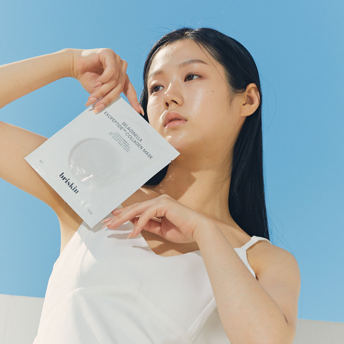 Woman holding BRISKIN Selaginella Exopeptide Collagen Mask 5 sheets against blue sky