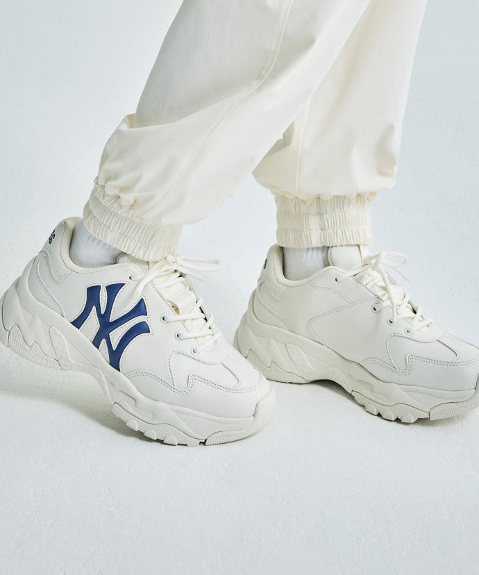 White sneakers with MLB Bigball CHUNKY Window NEW YORK YANKEES design, featuring navy logo, worn with cream pants on white background.
