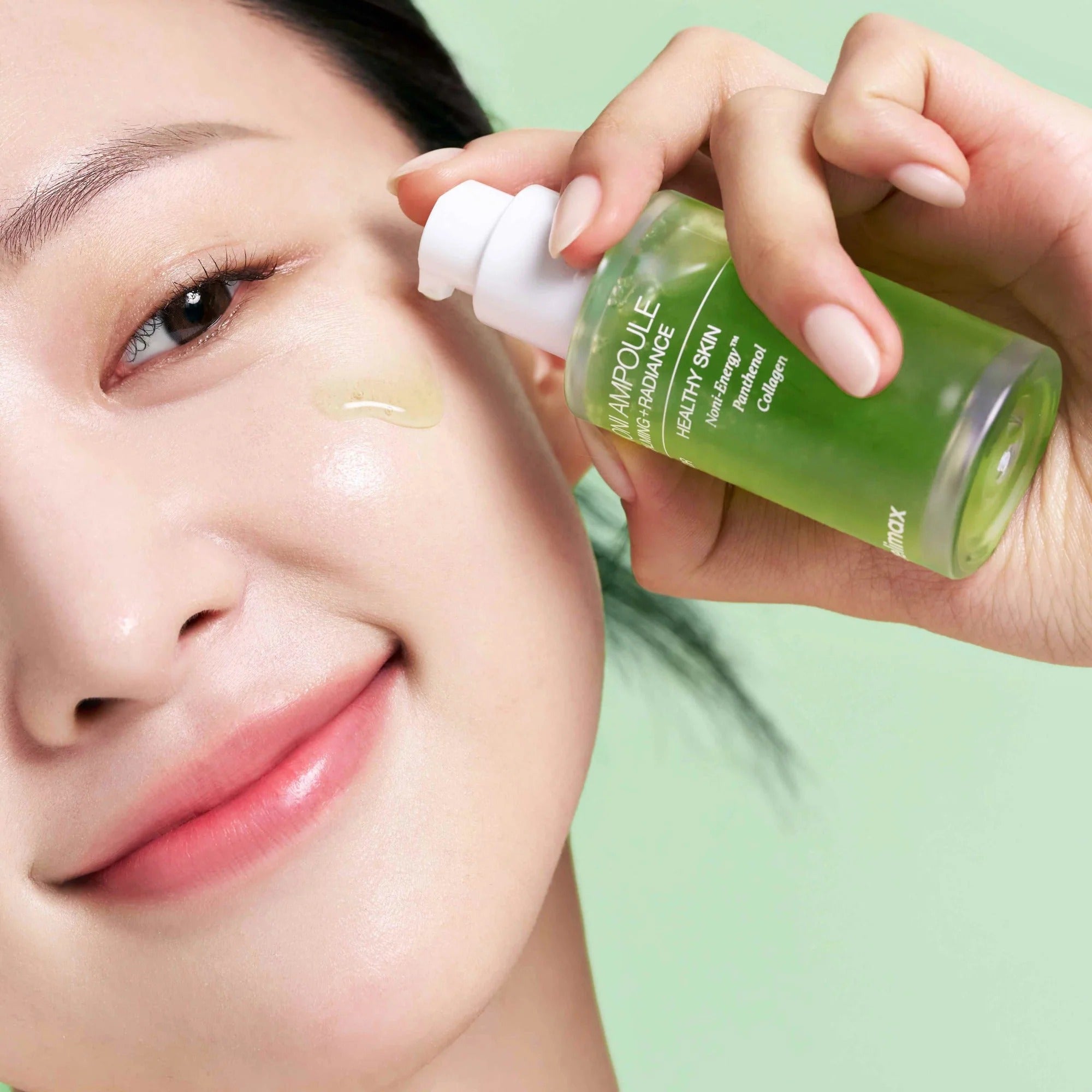 Smiling woman applying CELIMAX Noni Ampoule Calming+Radiance 100ml to her face for glowing skin.