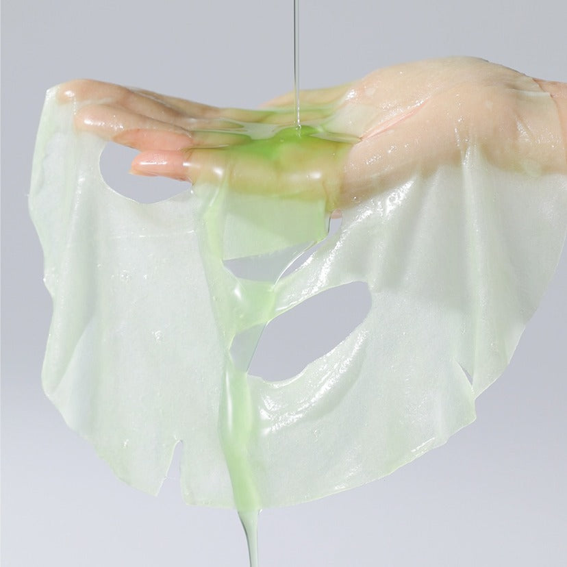 Hand holding CELIMAX Noni Ampoule Mask 10 Sheets with green serum dripping, showcasing the mask's moisturizing properties.