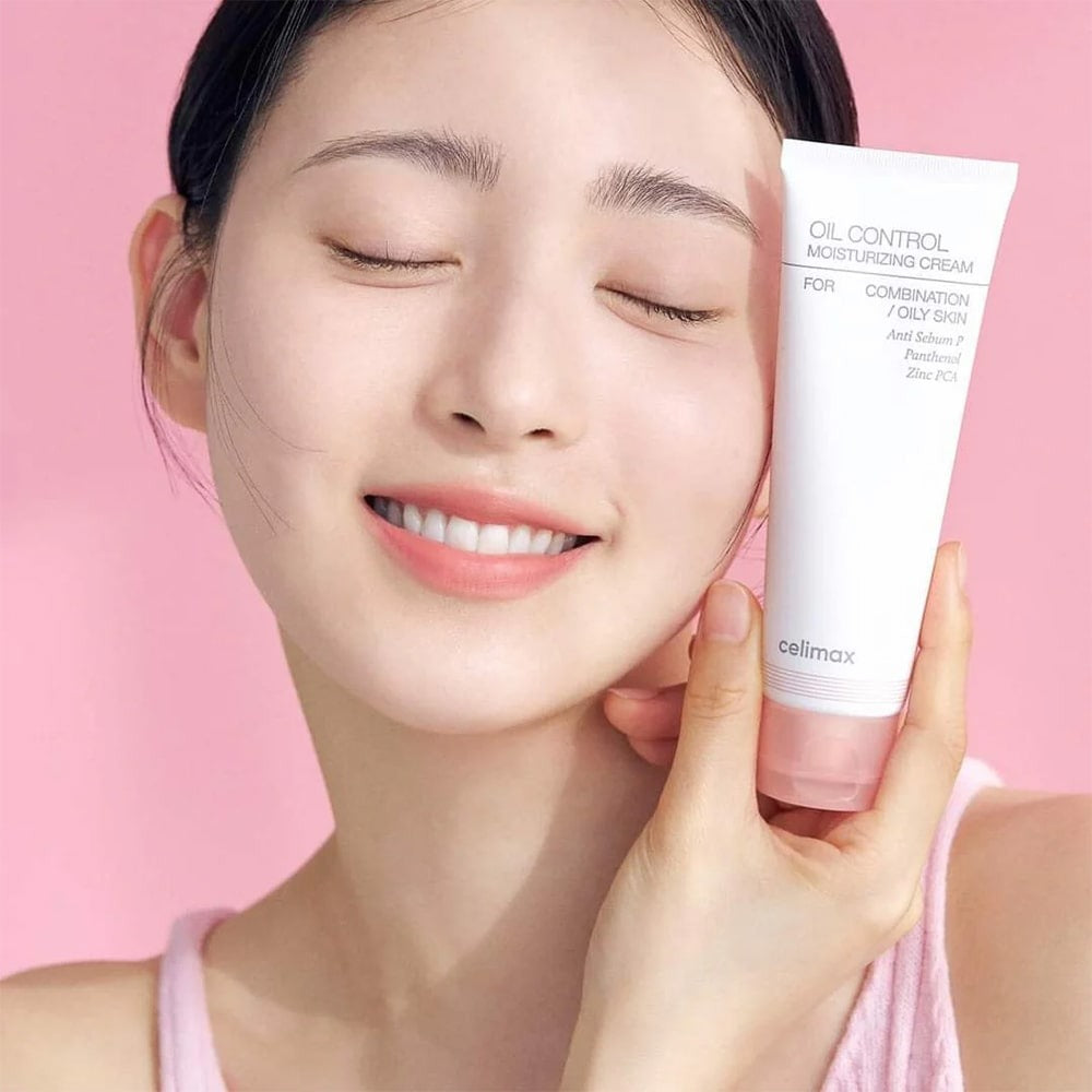 Smiling person holding CELIMAX Oil Control Moisturizing Cream 80ml, showcasing the product's packaging on a pink background.