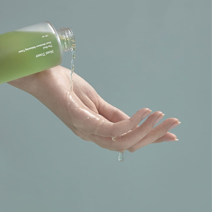 CELIMAX The Real Noni Moisture Balancing Toner 150ml being poured onto a hand, showcasing the texture and consistency of the product.