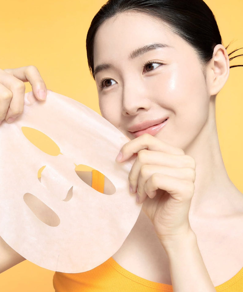 Woman holding CELIMAX Brightening Pore Blemish Cream Wrapping Mask 1 Sheets in front of yellow background