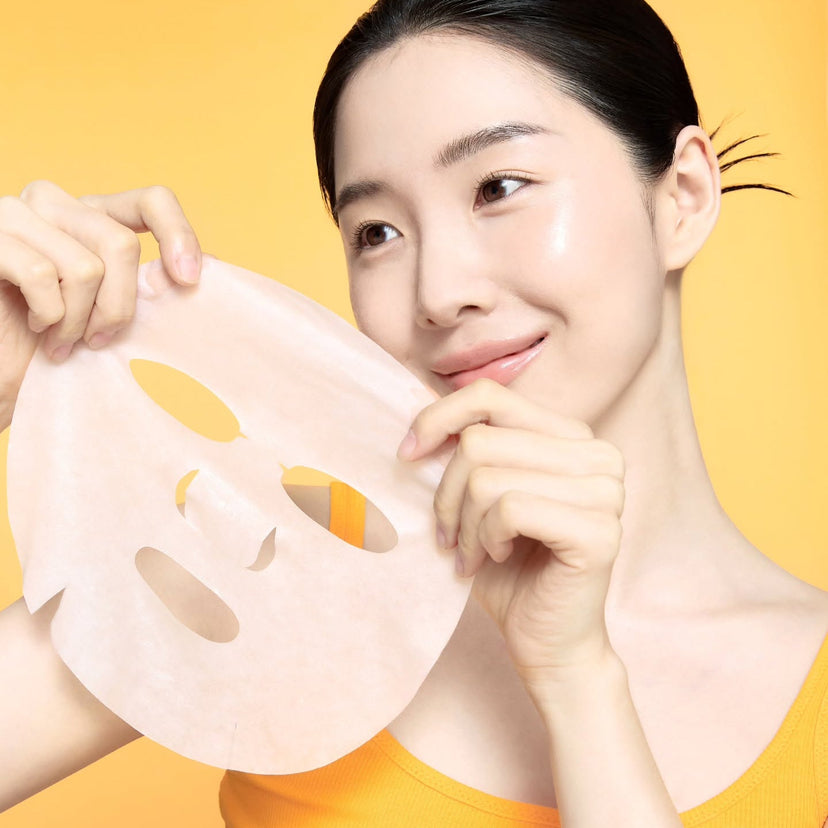 Woman holding CELIMAX Brightening Pore Blemish Cream Wrapping Mask 1 Sheets in front of yellow background