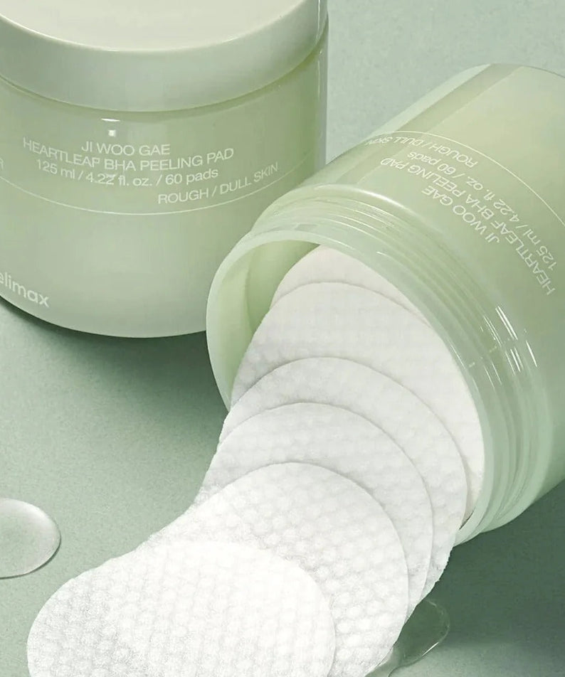 Open jar of CELIMAX Ji Woo Gae Heartleaf BHA Peeling Pad 60 Pads on green background, showcasing texture and packaging.