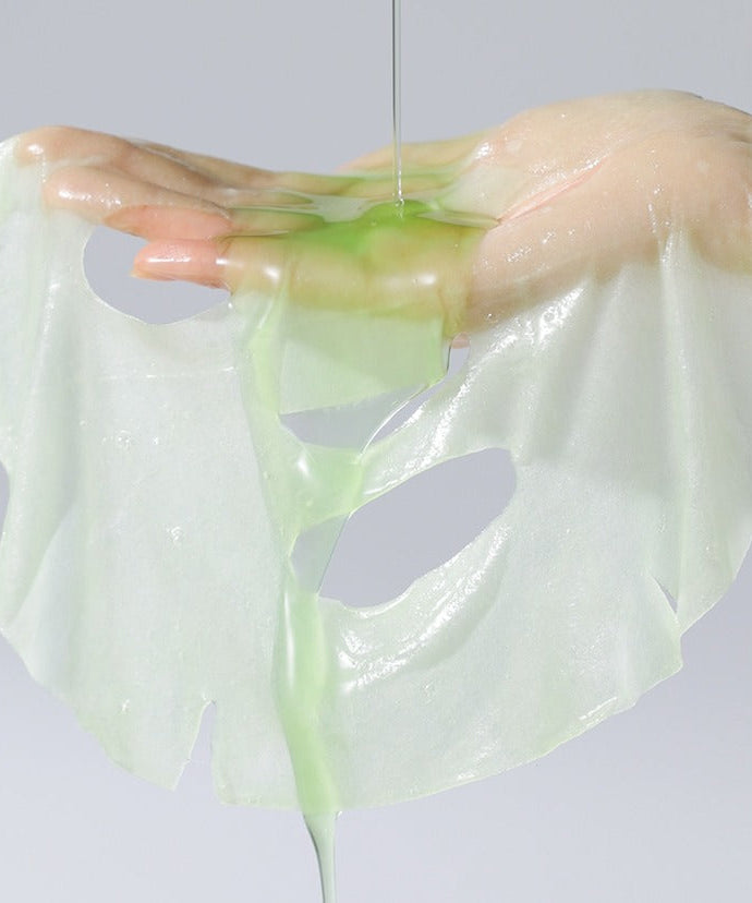 Hand holding CELIMAX Noni Ampoule Mask 10 Sheets with green serum dripping, showcasing the mask's moisturizing properties.