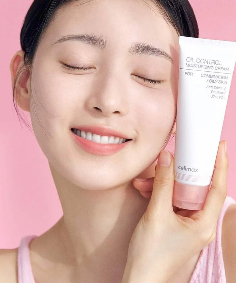 Smiling person holding CELIMAX Oil Control Moisturizing Cream 80ml, showcasing the product's packaging on a pink background.
