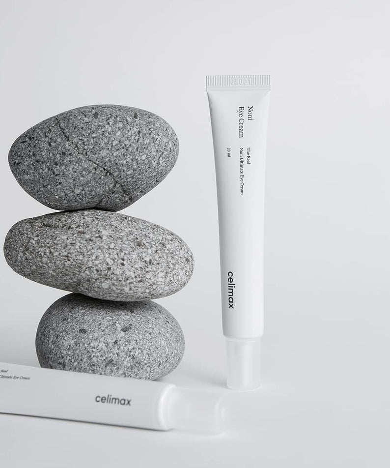 CELIMAX The Real Noni Ultimate Eye Cream 20ml tube displayed with stones for skincare product advertisement.