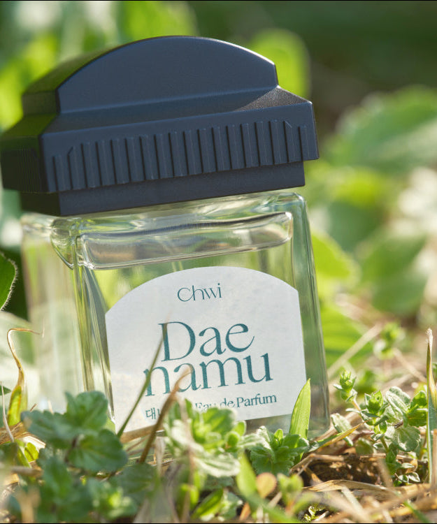 Bottle of CHWI (CHI) Eau De Parfume 50ml displayed outdoors on greenery.