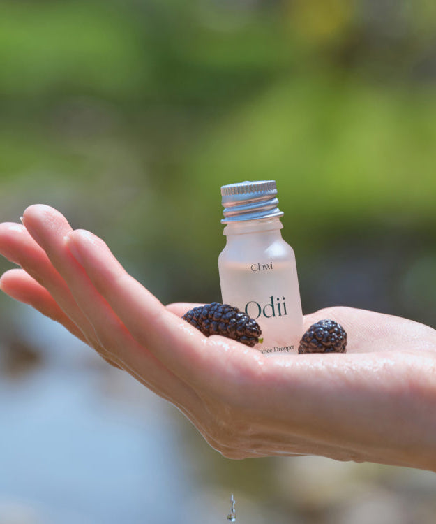 Hand holding CHWI (CHI) Odii Frangrance Dropper 10ml with natural scenery in the background.