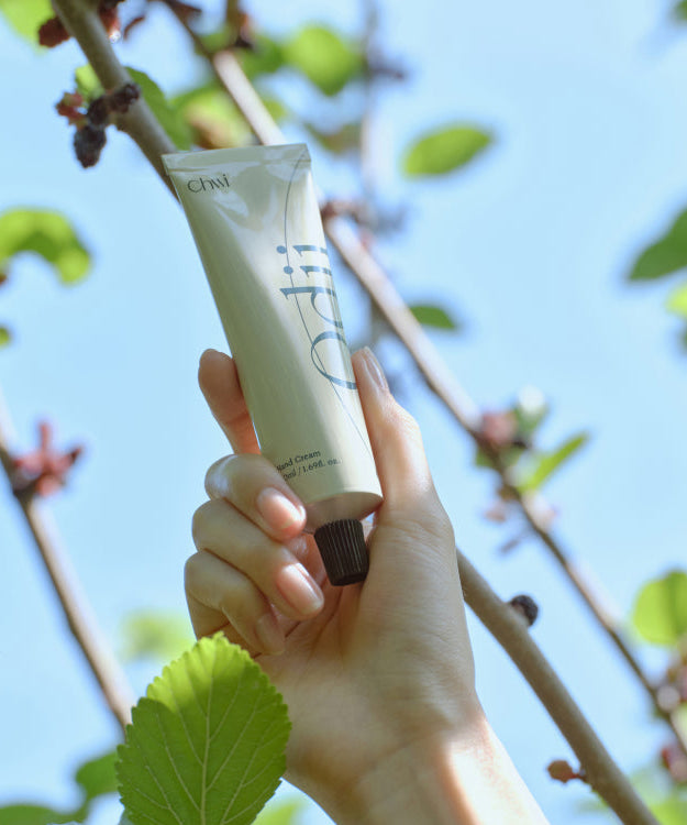 Hand holding CHWI (CHI) Odii Hand Cream 50ml with foliage background.