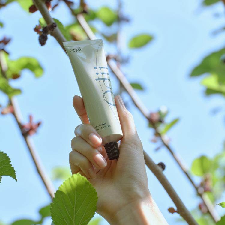 Hand holding CHWI (CHI) Odii Hand Cream 50ml with foliage background.