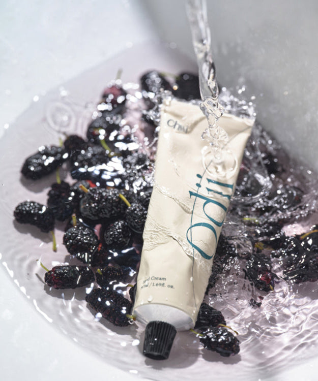 CHWI (CHI) Odii Hand Cream 50ml tube with flowing water, surrounded by fresh berries, highlighting the moisturizing blend and fragrance.