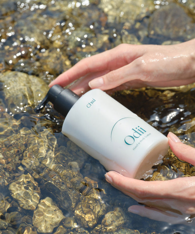Hands holding CHWI (CHI) Odii Hand & Body Lotion 300ml over clear water with rocks