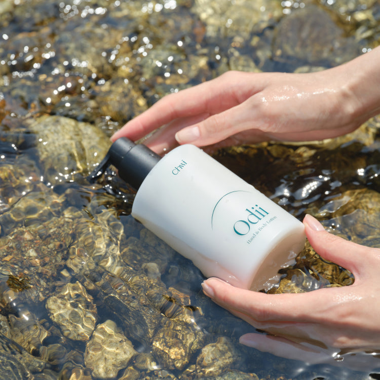 Hands holding CHWI (CHI) Odii Hand & Body Lotion 300ml over clear water with rocks