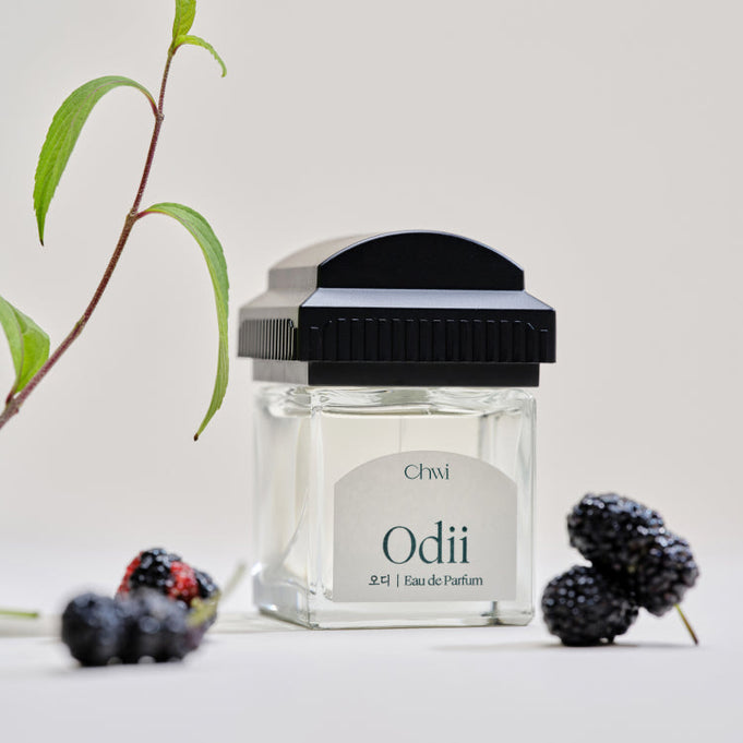 CHWI (CHI) Odii Parfume 50ml bottle surrounded by blackberries and green leaves on a neutral background.