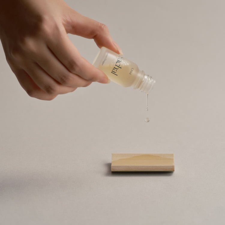CHWI (CHI) Sachak Fraangrance Dropper 10ml in use, aromatic liquid being dispensed from a small bottle onto a wooden block surface.