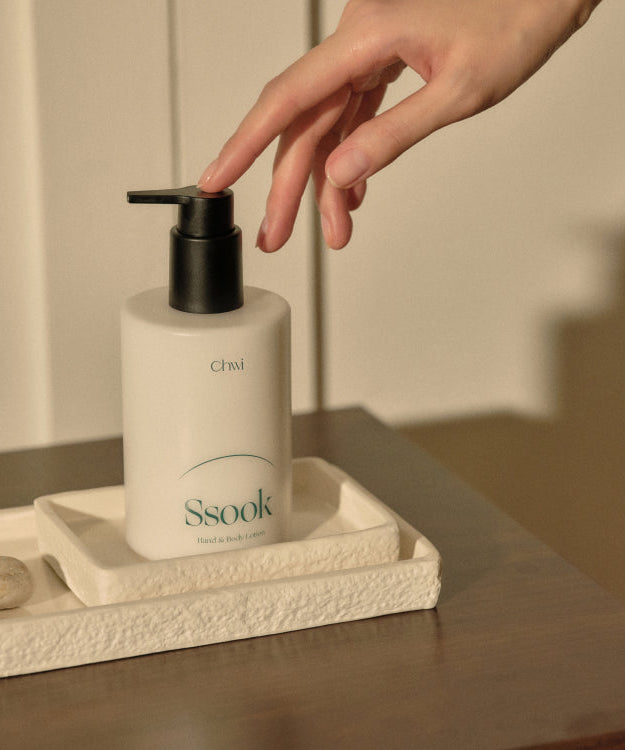 A hand reaching for CHWI (CHI) Ssook Hand & Body Lotion 300ml on a tray