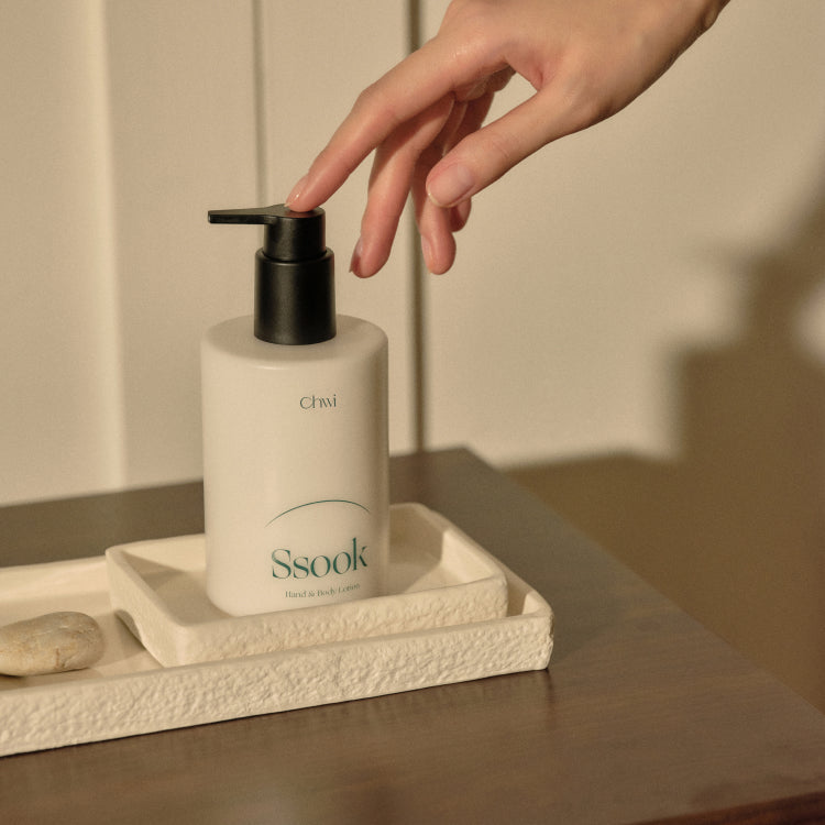 A hand reaching for CHWI (CHI) Ssook Hand & Body Lotion 300ml on a tray