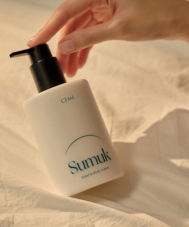CHWI (CHI) Sumuk Hand & Body Lotion 300ml on a bed with hand reaching for pump bottle