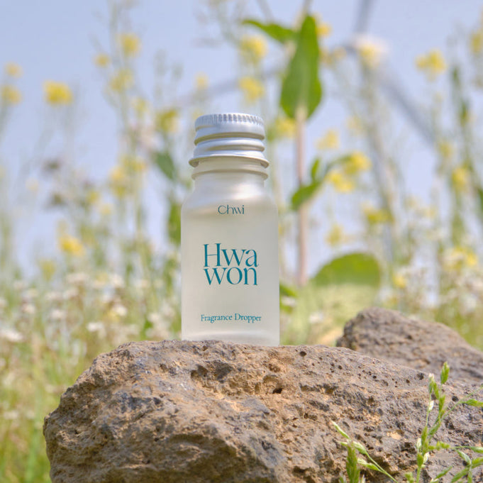CHWI (CHI) Wha Won Fragrance Dropper 10ml bottle on a rock in a meadow setting with wildflowers in the background.