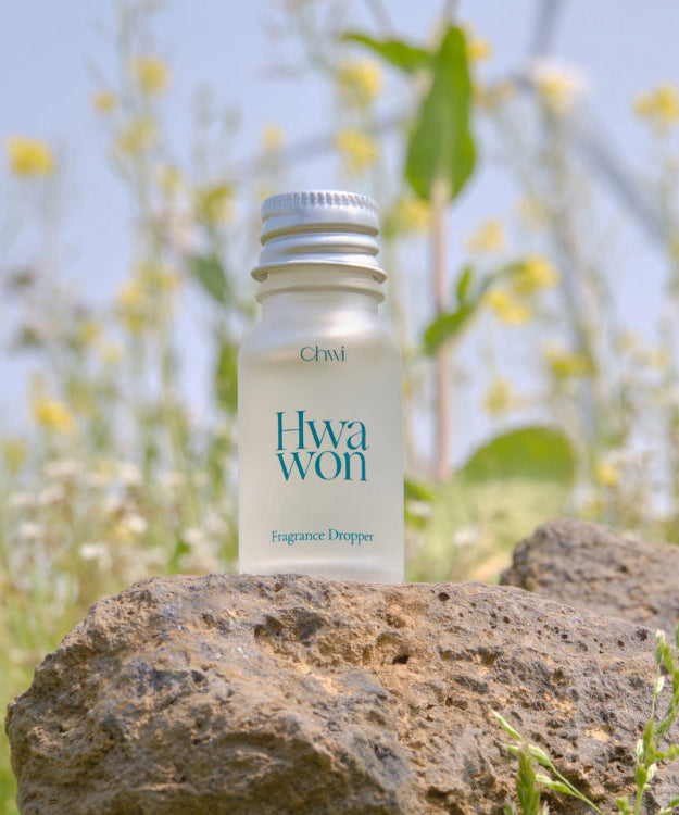 CHWI (CHI) Wha Won Fragrance Dropper 10ml bottle on a rock in a meadow setting with wildflowers in the background.