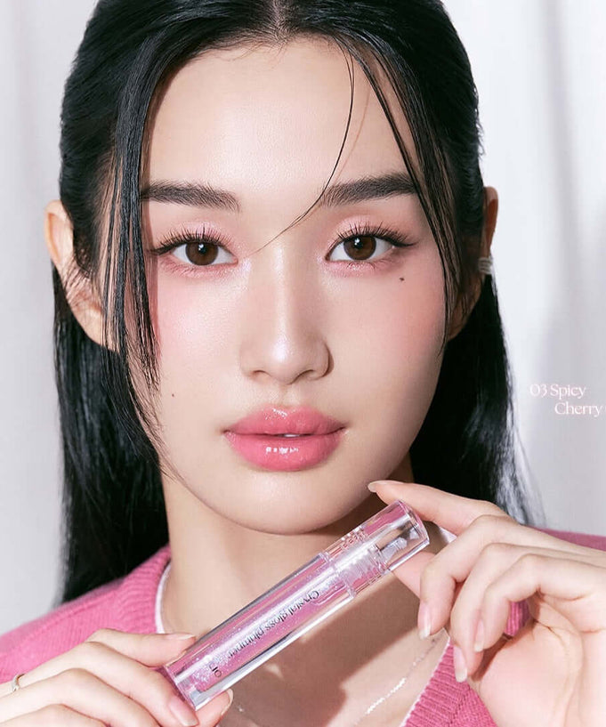 Woman holding CLIO Crystal Gloss Plumper with shiny lips, highlighting the lip-enhancing properties of the product.