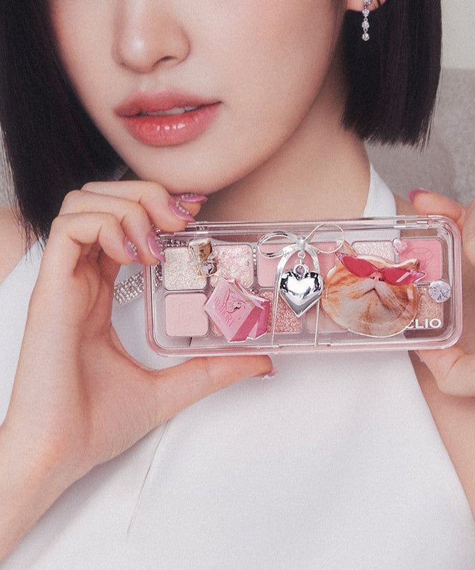 Woman holding CLIO Pro Eye Palette Air (#01 to #15) with pink and brown shades, featuring a decorative charm.