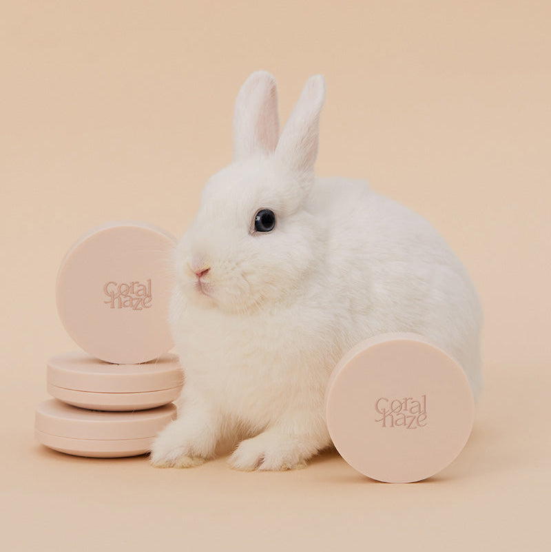 Cute rabbit with CORALHAZE Fixing Blur Cushion SPF50 PA++++ 13g on display, showcasing its soft beige packaging.