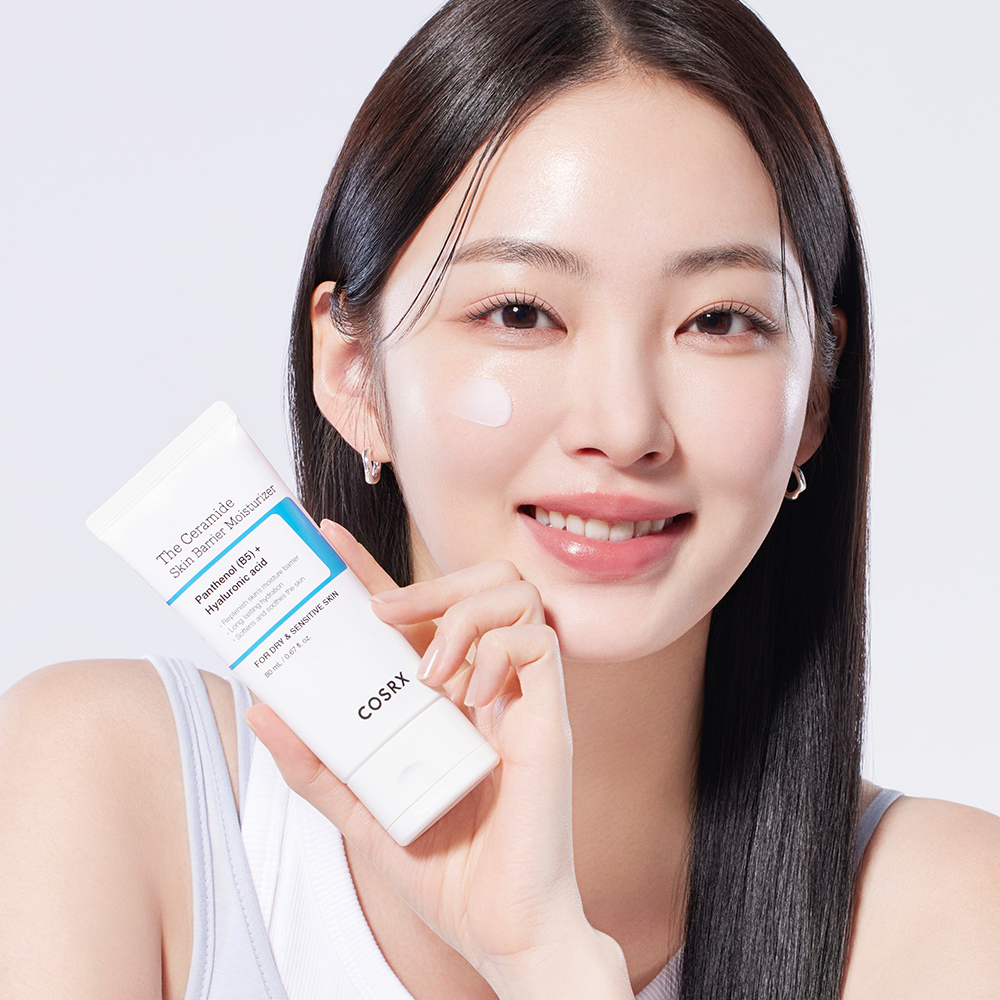 Woman applying COSRX The Ceramide Skin Barrier Moisturizer to her face, holding the product in hand.
