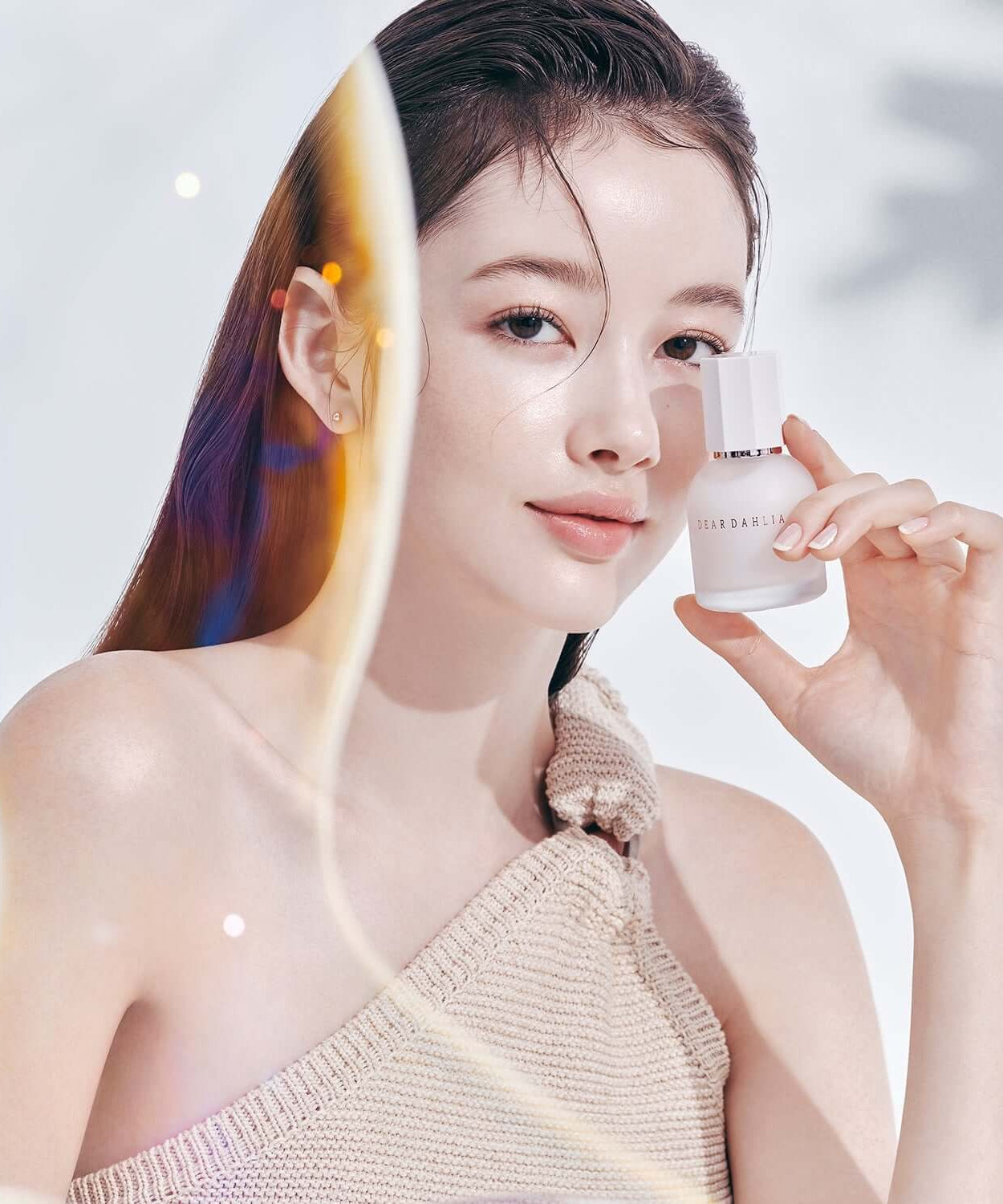 Woman holding DEAR DAHLIA Prime Layer Skin Prep bottle against a soft background