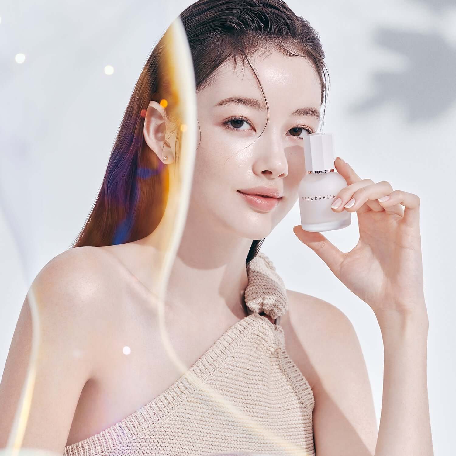 Woman holding DEAR DAHLIA Prime Layer Skin Prep bottle against a soft background