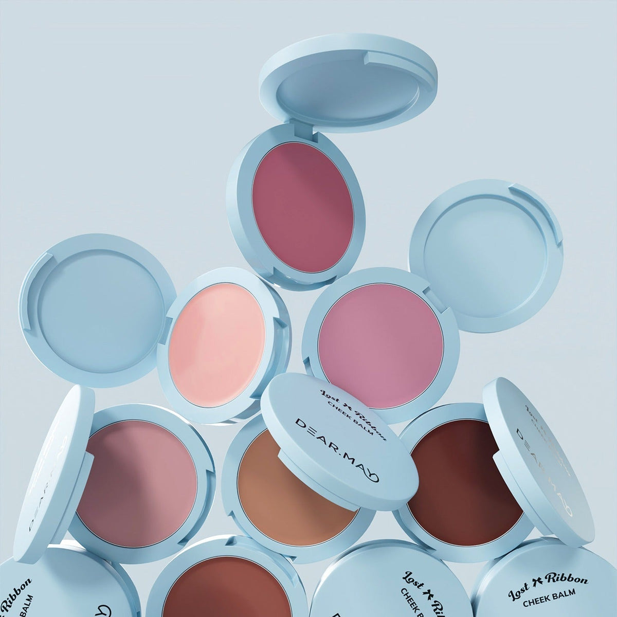 Open compacts displaying DEAR MAY Lost Ribbon Check Balm in various shades of pink and brown, showcasing elegant packaging and color range.