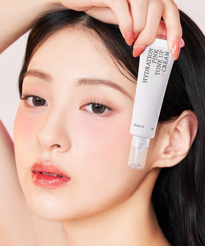 Woman holding DEAR.A Hydration Pink Tone-Up Cream 30ml bottle near face with glowing skin.