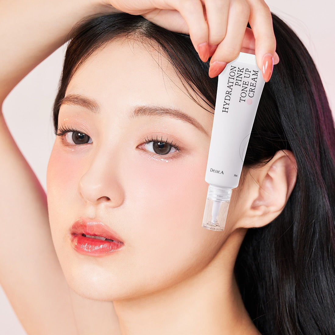 Woman holding DEAR.A Hydration Pink Tone-Up Cream 30ml bottle near face with glowing skin.