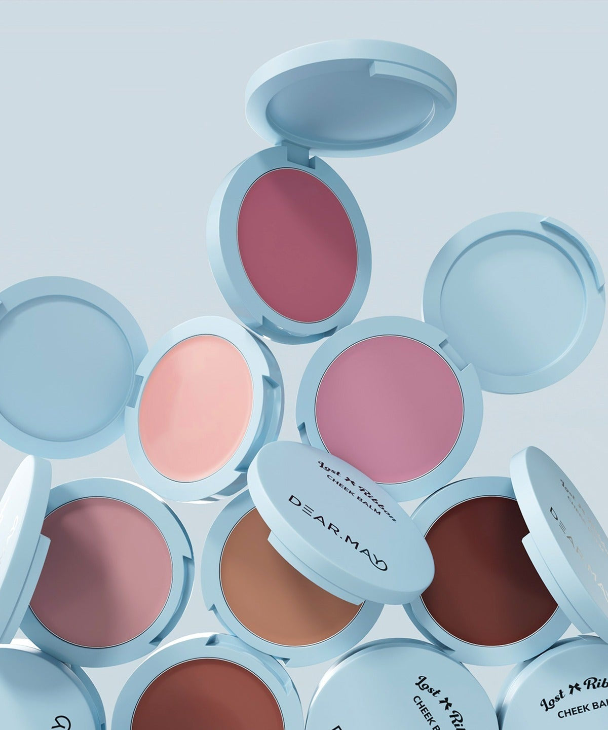 Open compacts displaying DEAR MAY Lost Ribbon Check Balm in various shades of pink and brown, showcasing elegant packaging and color range.