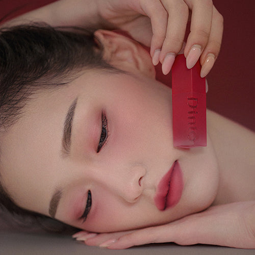 Model holding DINTO Blurring Lip Veil in red shade, showcasing smooth lip and facial complexion, highlighting beauty and elegance.