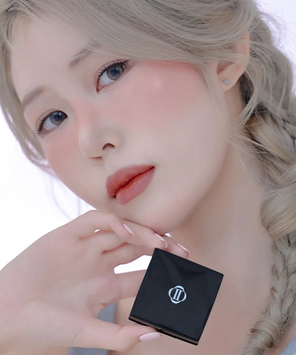 Model holding DINTO Be My Wendy Blusher with natural makeup and braided hair.